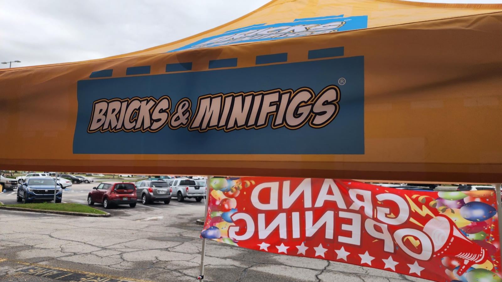 Bricks and Minifigs branded tent with Grand Opening banner in the parking lot